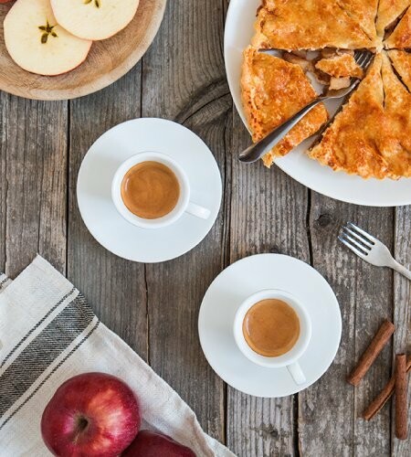 Two cups of espresso with apple pie slices on a rustic table.